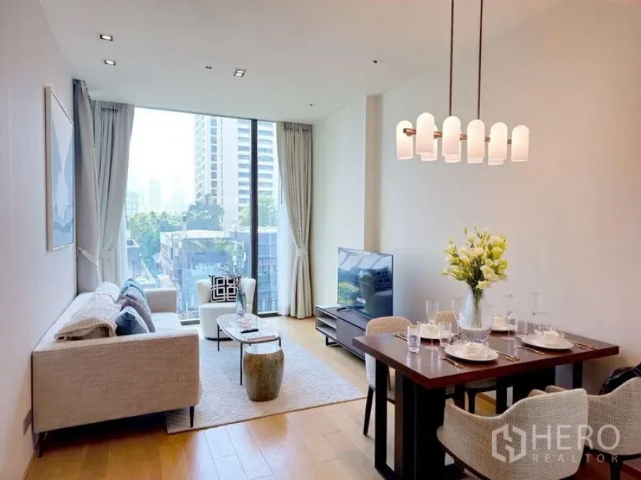Condominium for rent or sale in Pathum Wan, Bangkok - Open-plan living and dining area with chandelier, TV console, and floor-to-ceiling window.