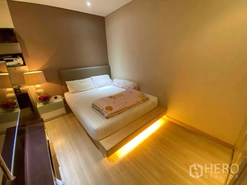 公寓 出租在Ratchathewi, Bangkok - 次卧配平台床、暖色床下灯、床头柜与置物架。