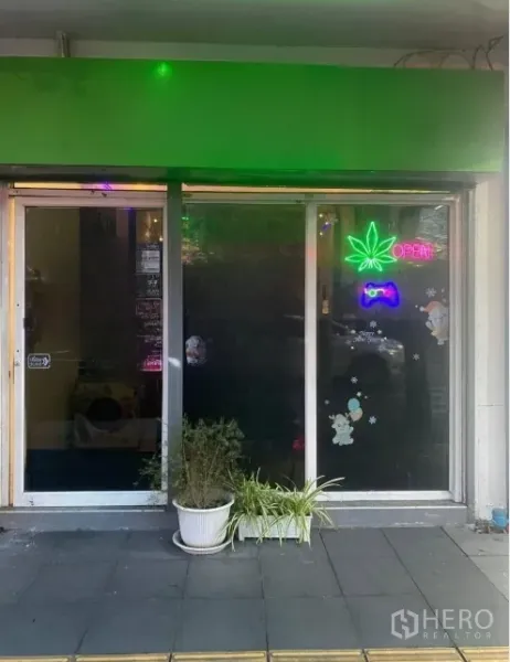 店屋 出租或出售在Khlong Toei, Bangkok - 临街玻璃店面与推拉门，绿色檐篷，霓虹叶形“OPEN”标志和门前花盆。