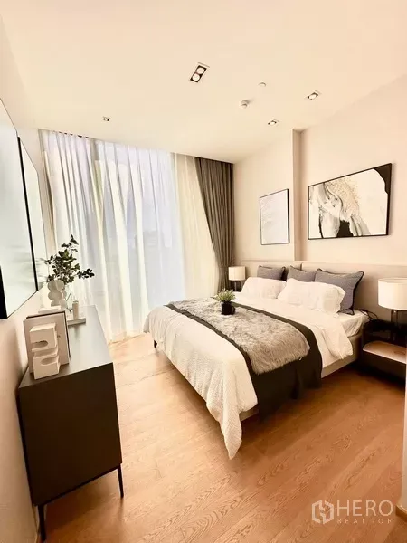 Condominium for rent in Pathum Wan, Bangkok - Primary bedroom with a large window, neutral decor, and a plush bed with bedside tables.