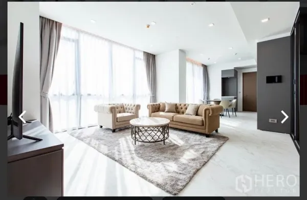 Condominium for rent or sale in Watthana, Bangkok - Open-plan living area showing sofa set, round coffee table and kitchen beyond.
