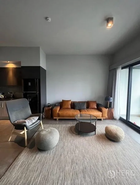 Condominium for rent in Watthana, Bangkok - Bright lounge with floor-to-ceiling windows, tan sofa, accent chair and round coffee table.