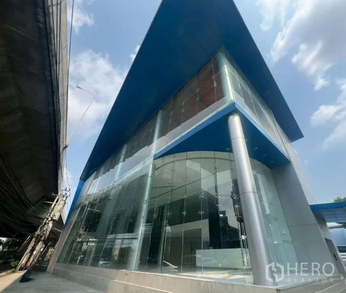 展厅 出租 - 转角地块的现代玻璃幕墙展示厅外观，配蓝色挑檐屋顶。