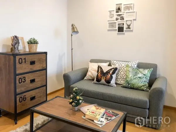 คอนโด ให้เช่าหรือขายในBang Rak, Bangkok - มุมพักผ่อนพร้อมโซฟา ตู้ไม้สไตล์อินดัสเทรียล โคมไฟยืน และกรอบรูปบนผนัง