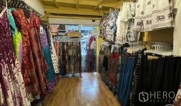 零售空间 出租在Watthana, Bangkok - 狭长型店铺内部，彩色服装挂架、瓷砖地面与玻璃入口。