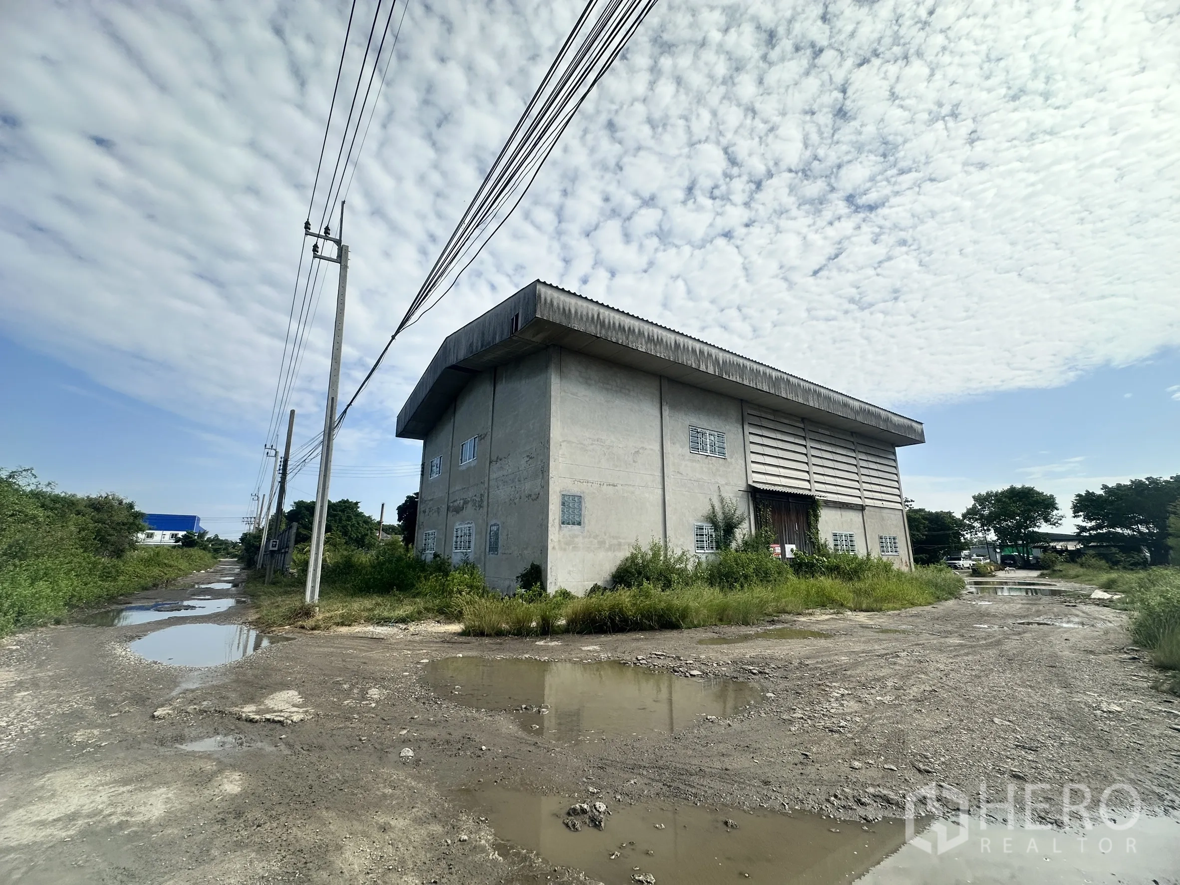 Land for sale in Mueang Samut Prakan, Samut Prakan - Corner perspective of the warehouse next to power lines and a rough access road.