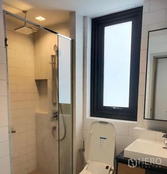 Condominium for rent in Chatuchak, Bangkok - Second bathroom featuring a rain shower, glass cubicle, large frosted window, and sleek vanity.