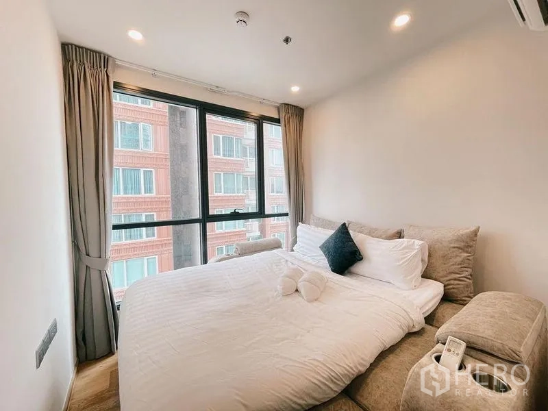 คอนโด ให้เช่าในRatchathewi, Bangkok - ห้องนอนที่สองพร้อมเตียง ม้านั่งบุนวม และหน้าต่างบานกว้างมองอาคารใกล้เคียง