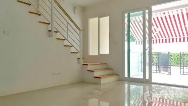 Townhouse for rent in Wang Thonglang, Bangkok - Bright living area with glossy tile floors, white-railed staircase, and sliding glass doors to the front patio.