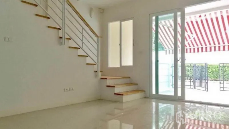 Townhouse for rent in Wang Thonglang, Bangkok - Bright living area with glossy tile floors, white-railed staircase, and sliding glass doors to the front patio.