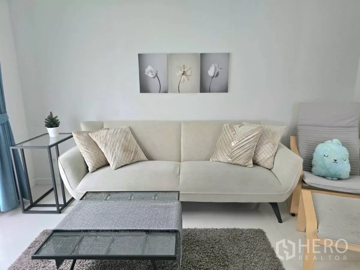 Detached House for rent in Samut Prakan - Light-toned living room with sofa, coffee table and simple wall art.