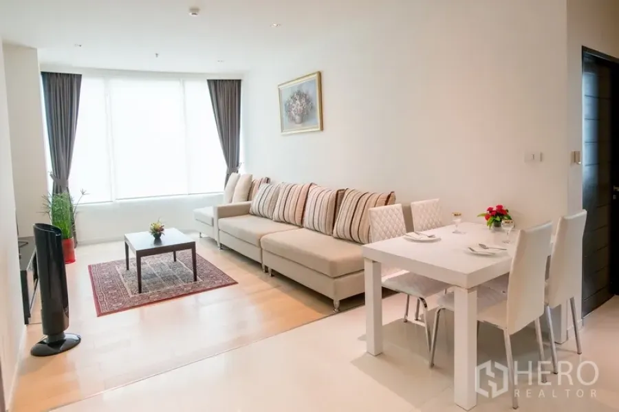 Condominium for rent in Watthana, Bangkok - Bright living and dining area with a large sectional sofa, white dining table, and floor-to-ceiling windows.