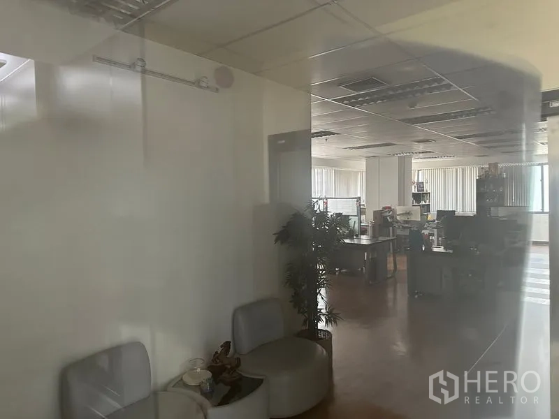 办公空间 出租在Bang Rak, Bangkok - 透过玻璃隔断看到开放式办公区，设有工位、吊顶照明、竖百叶与小型等候区。