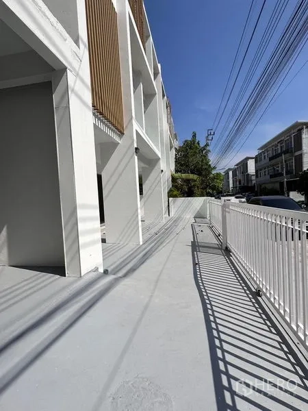Home Office for sale in Lat Krabang, Bangkok - Front driveway and walkway beside a gated townhouse row under a clear blue sky.