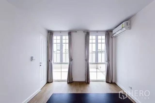 Townhouse for rent in Watthana, Bangkok - Sunlit room with two tall French windows, curtains and wall-mounted air conditioner.