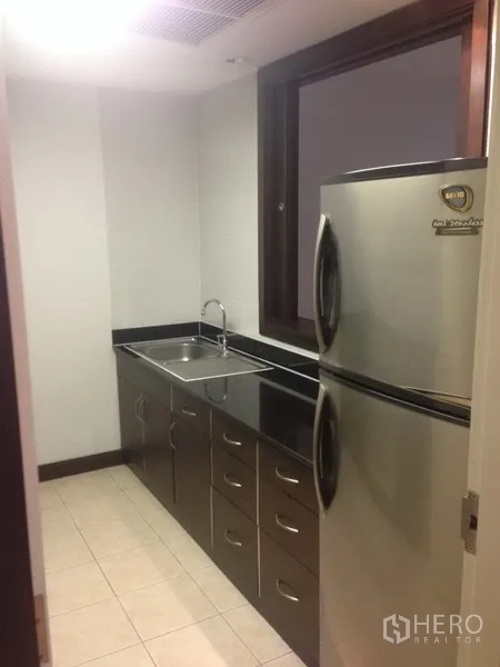 Condominium for rent in Pathum Wan, Bangkok - Service kitchen with stainless-steel fridge, sink and black granite countertop.