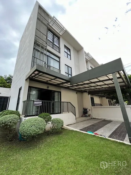 联排别墅 出租在Saphan Sung, Bangkok - 现代三层联排外观，带车棚、草坪与修剪整齐的灌木。