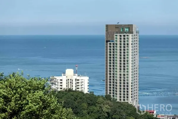 公寓 出租或出售在Si Racha, Chon Buri - 临海高层公寓外观，远眺蓝色海面与绿色山坡。