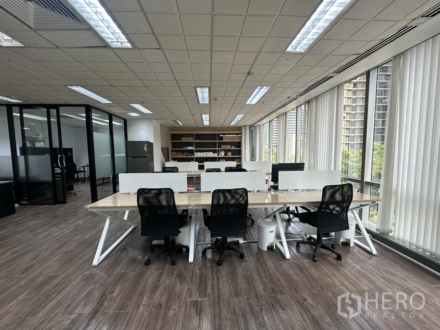 Office Space for rent - Rows of workstations with task chairs beside floor-to-ceiling windows for ample daylight.