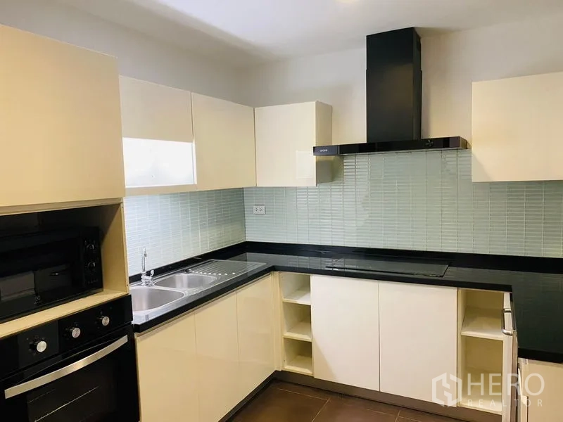 Condominium for rent in Watthana, Bangkok - U-shaped kitchen with white cabinetry, black stone countertops, and tiled backsplash with range hood.