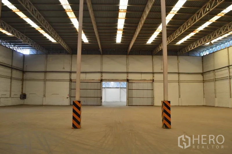 Warehouse for rent in Bang Sue, Bangkok - Open storage hall with central columns, bright roof panels and wide sliding gates for easy movement of goods.