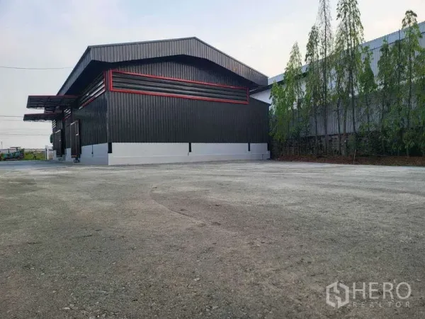 Warehouse for rent in Sam Phran, Nakhon Pathom - Rear view of the warehouse with a large paved yard and trees for easy truck parking and turning.