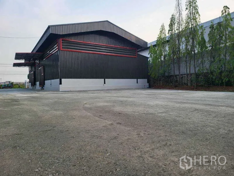 Warehouse for rent in Sam Phran, Nakhon Pathom - Rear view of the warehouse with a large paved yard and trees for easy truck parking and turning.