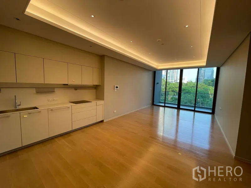 Condominium for rent or sale in Pathum Wan, Bangkok - Open-plan living and kitchen with light wood floors, recessed lighting and full-height glass doors to a balcony with city and garden views.