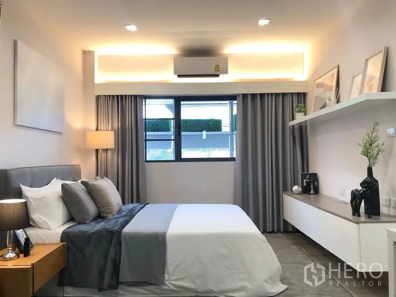 Shophouse for rent in Lat Phrao, Bangkok - Modern bedroom with soft cove lighting, grey accents, floating shelf and curtained window.