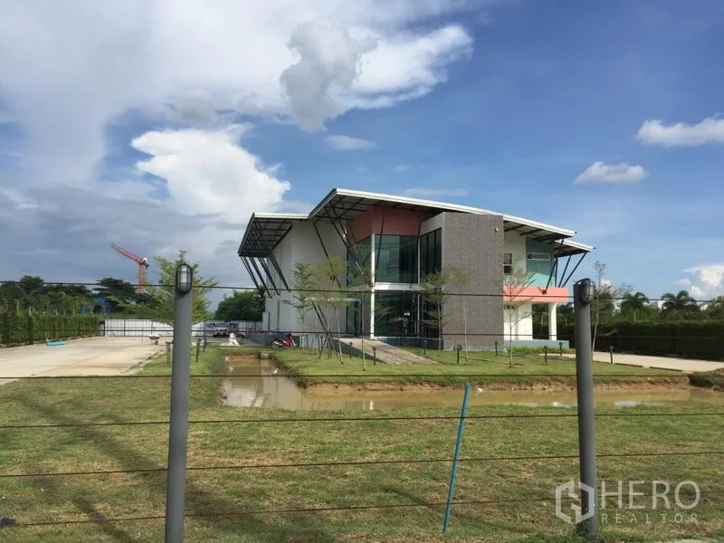 โรงงาน ให้เช่าในLam Luk Ka, Pathum Thani - อาคารสำนักงานโรงงานสมัยใหม่ ภายนอกพร้อมสนามหญ้า ทางเข้าคอนกรีต และบ่อพักน้ำ ในอำเภอลำลูกกา ปทุมธานี ใต้ท้องฟ้าโปร่ง