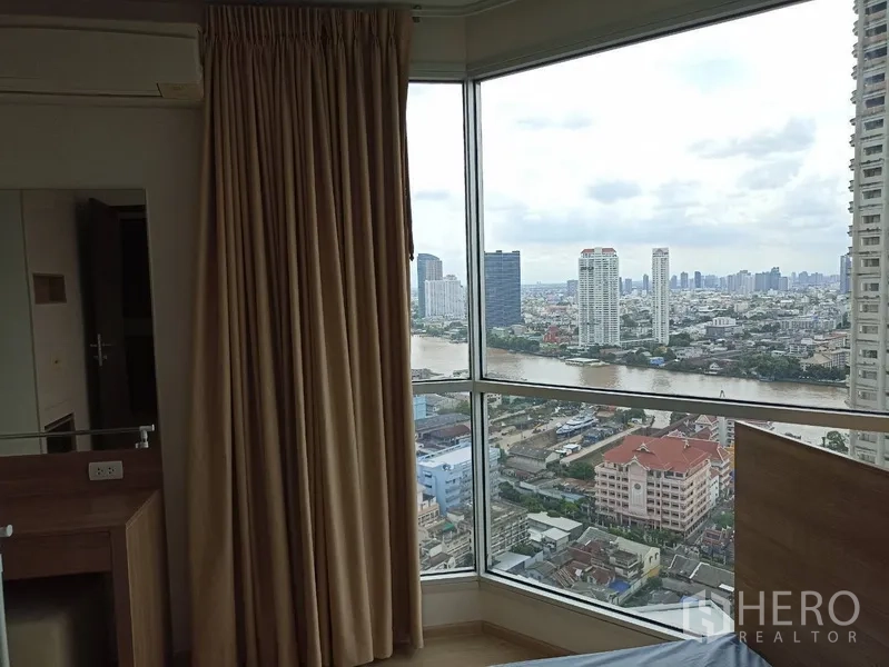 Condominium for rent or sale in Sathon, Bangkok - Bedroom corner windows framing river and skyline views with beige curtains.