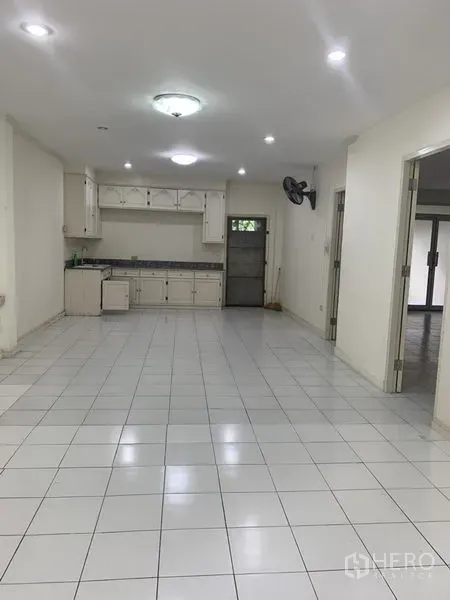 Townhouse for rent in Wang Thonglang, Bangkok - Open-plan living and dining area with white tiles, ceiling lights and a simple built-in kitchen.