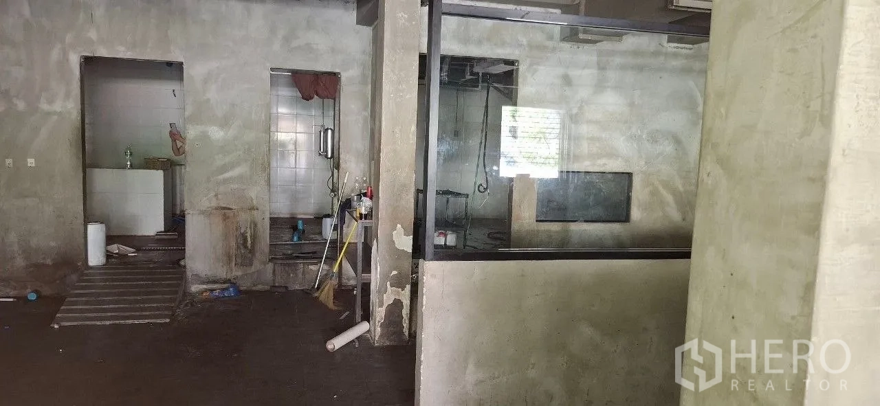 店屋 出租或出售在Watthana, Bangkok - 水泥裸墙的室内，大型玻璃隔断与两处通往瓷砖后场的门洞。