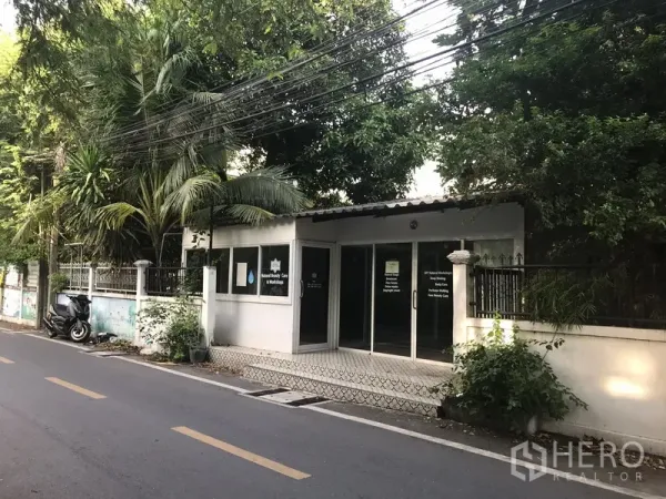 零售空间 出租在Khlong Toei, Bangkok - 街边零售店面，整面玻璃门与瓷砖门廊，绿树环绕，位于Phra Khanong安静小巷，临近轻轨站。