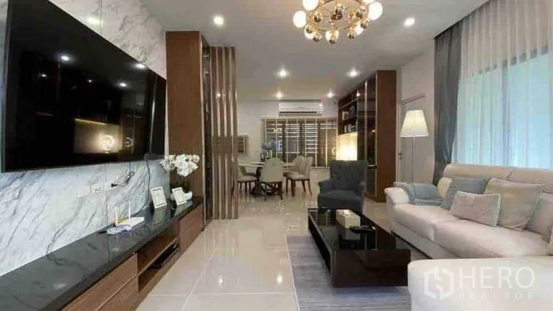 Detached House for rent or sale in Prawet, Bangkok - Open-plan living room with marble TV wall, chandelier and dining set.