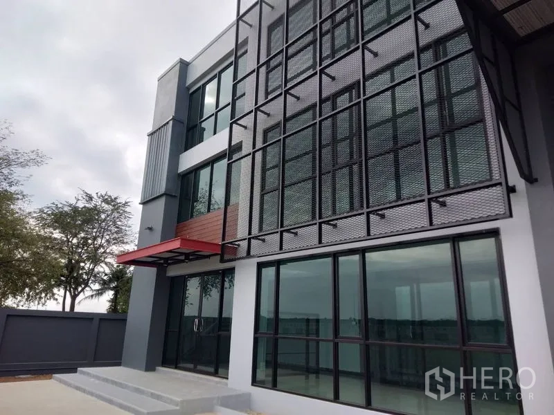 โรงงาน ให้เช่าหรือขายในLam Luk Ka, Pathum Thani - มุมใกล้ด้านหน้าพร้อมกระจกเต็มผนัง ซันสกรีนเหล็ก และกันสาดสีแดง