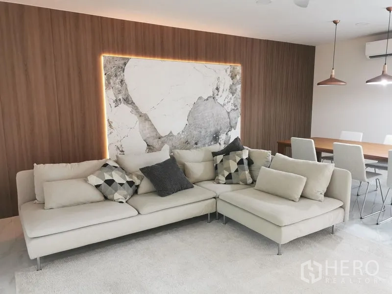 Townhouse for rent in Bang Phli, Samut Prakan - Cozy living area featuring L-shaped sofa, wood accent wall with illuminated marble panel.