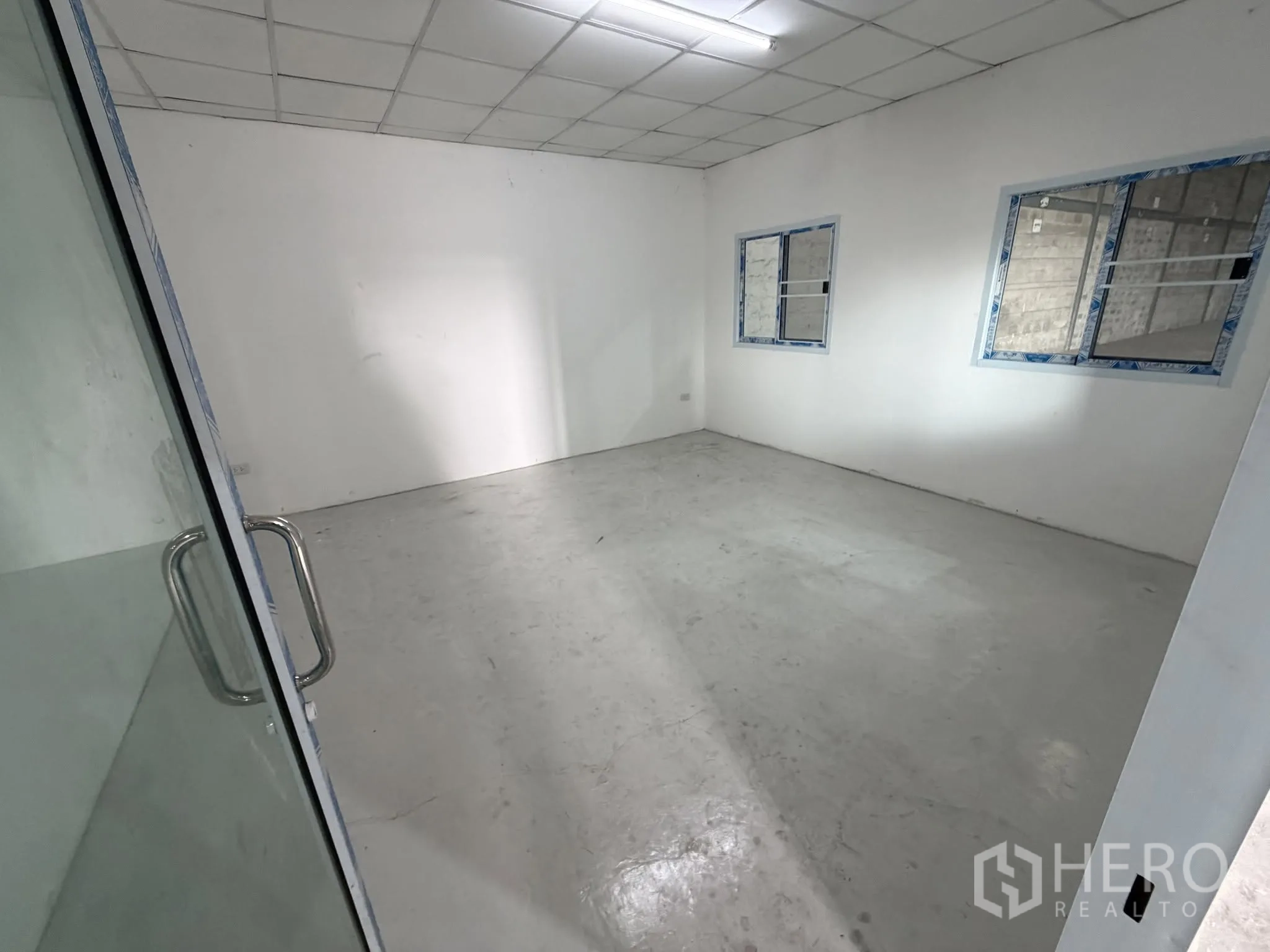 Warehouse for rent in Bang Na, Bangkok - Enclosed office room with glass door, windows, and overhead lighting inside the warehouse.