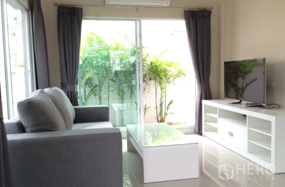 Detached House for rent in Saphan Sung, Bangkok - Bright living room with gray sofa, TV console and sliding doors opening to a small garden