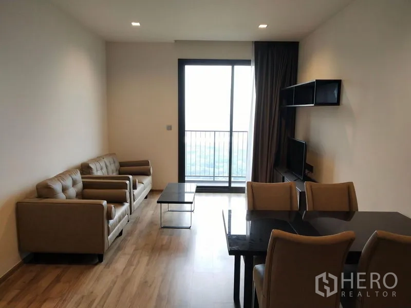 Condominium for rent in Chatuchak, Bangkok - Bright living and dining room with sofa set, dining table, TV shelf, and sliding glass door to the balcony.