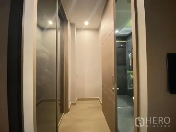 Condominium for rent in Huai Khwang, Bangkok - Hallway with mirrored wardrobe doors leading to a modern bathroom with a glass-enclosed shower.