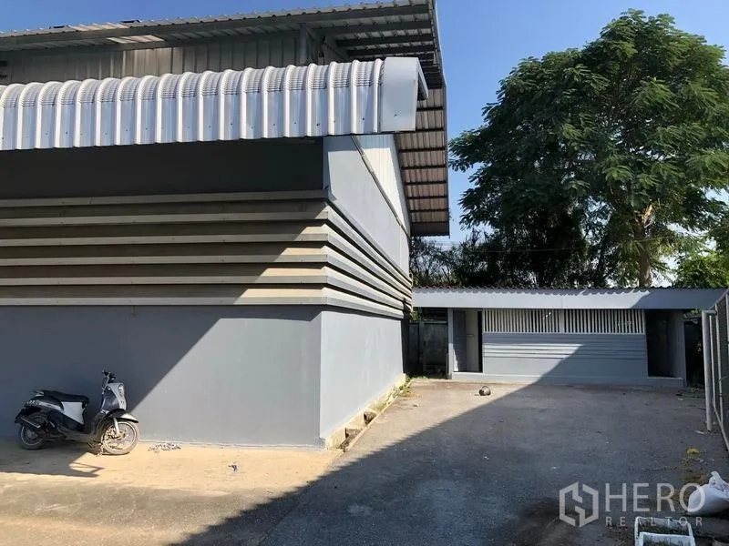 工厂 出租在Bang Bua Thong, Nonthaburi - 工厂转角处，侧巷、成树与一座附属小建筑。