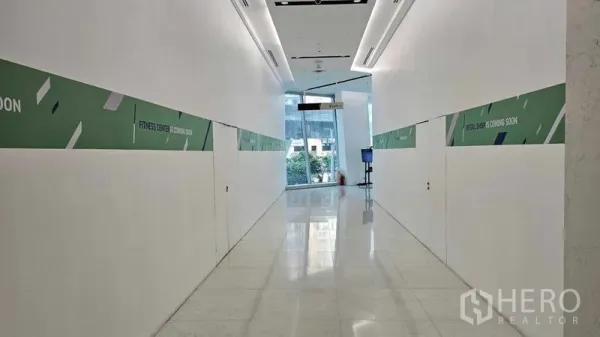 零售空间 出租 - 明亮的商业走廊，白色抛光地面与指示牌，通往玻璃大堂。