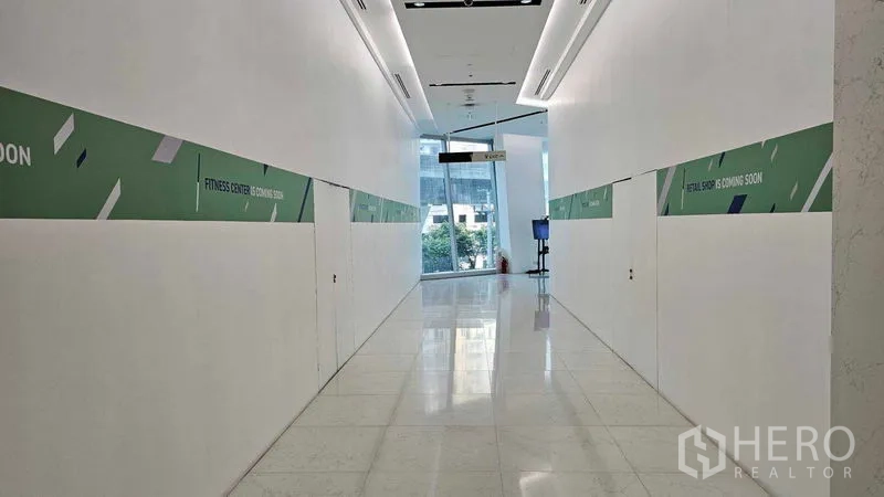 零售空间 出租 - 明亮的商业走廊，白色抛光地面与指示牌，通往玻璃大堂。