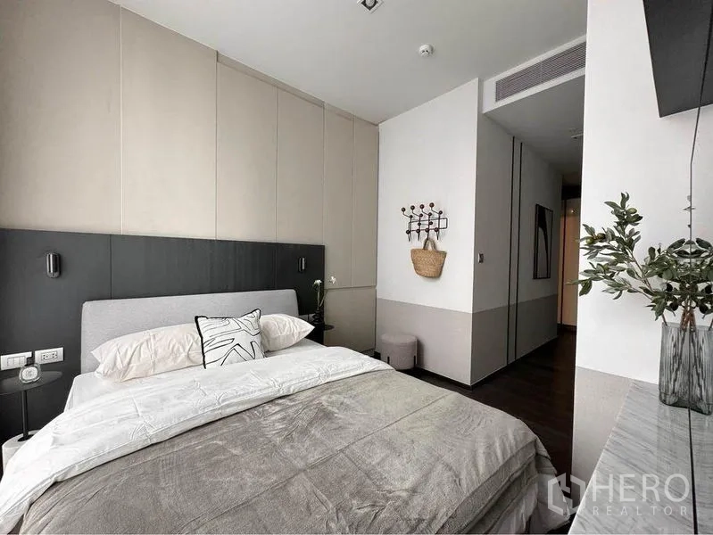Condominium for rent or sale in Watthana, Bangkok - Modern bedroom with paneled wall, double bed, hallway entry and console with plant.