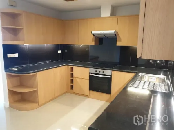 Condominium for rent in Watthana, Bangkok - L-shaped kitchen with light wood cabinetry, black stone countertops and backsplash, built-in oven and range hood.