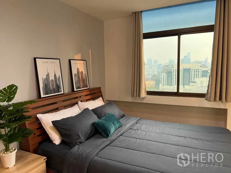 Condominium for rent in Ratchathewi, Bangkok - Primary bedroom with wooden bed, framed artwork, and a large window overlooking the Bangkok skyline.