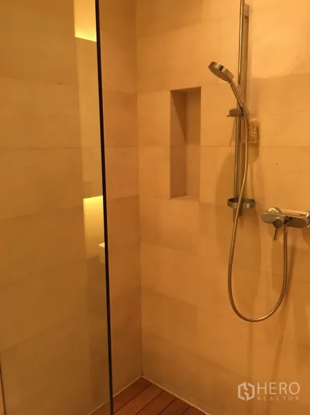 公寓 出租或出售在Bang Rak, Bangkok - 步入式淋浴间，手持花洒、玻璃隔断、内置置物槽与暖色石材墙面。