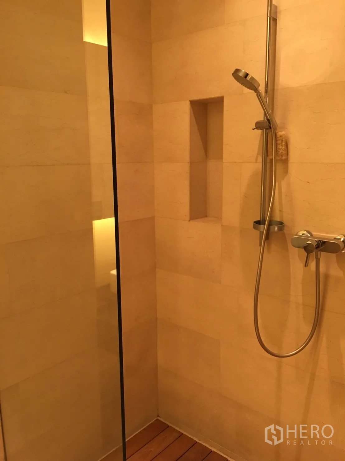 公寓 出租或出售在Bang Rak, Bangkok - 步入式淋浴间，手持花洒、玻璃隔断、内置置物槽与暖色石材墙面。