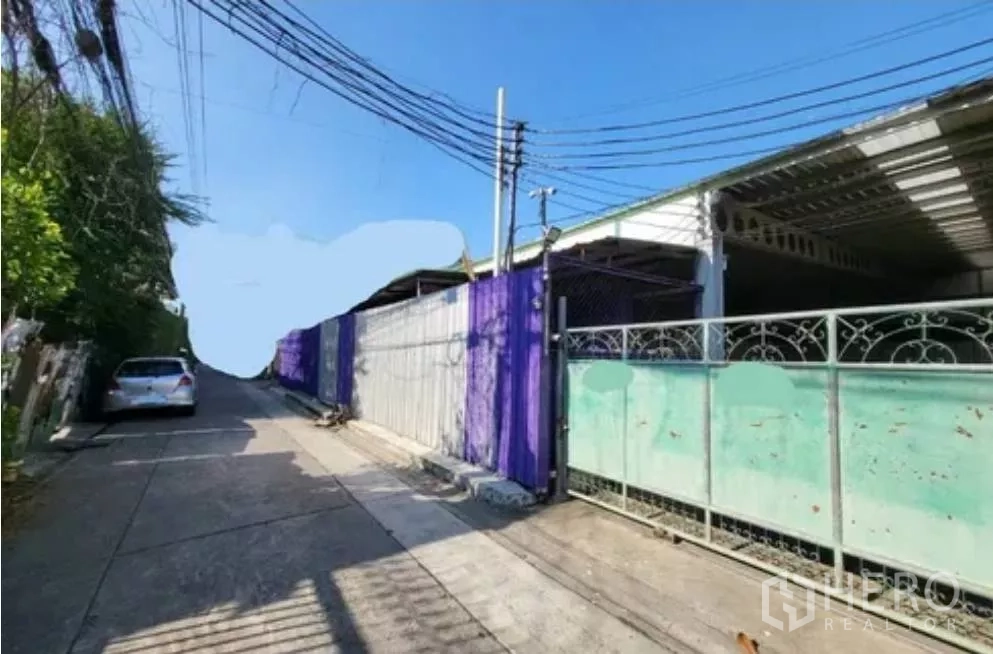 Warehouse for rent in Din Daeng, Bangkok - Gated warehouse frontage on a narrow lane with overhead power lines, suitable for small pickups.